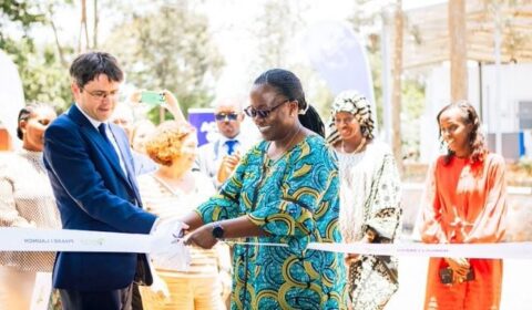 A man in a suit and a woman in colorful attire cut a ribbon at an outdoor ceremony, while several people watch and take photos in the background.