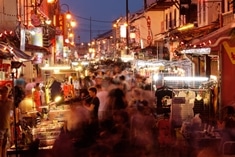 A crowded night market with bright lights, food stalls, and people shopping along a busy street lined with buildings.
