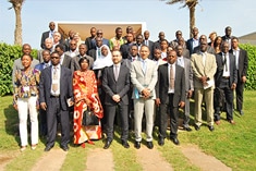 A group of people in business attire pose outdoors for a group photo, standing on grass with greenery and palm trees in the background.