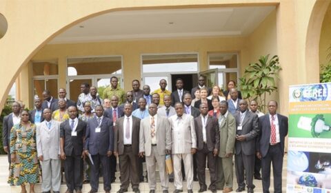 A large group of people in formal attire pose for a photo outside a building; a poster promoting energy and environment is visible on the right side.