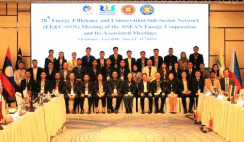 A large group of people in business attire pose for a photo in front of a screen displaying the title of an ASEAN Energy meeting, with flags from various countries on both sides.