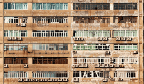 A close-up view of an old apartment building facade with many windows, air conditioning units, and visible weathering and peeling paint.