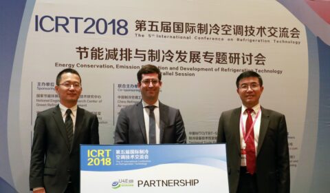 Three men in suits stand and smile behind a sign at the ICRT2018 conference on refrigeration technology, showcasing partnerships for energy conservation and emission reduction.
