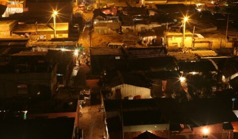 A nighttime aerial view of a densely packed urban area with dim streetlights illuminating narrow streets and small buildings.