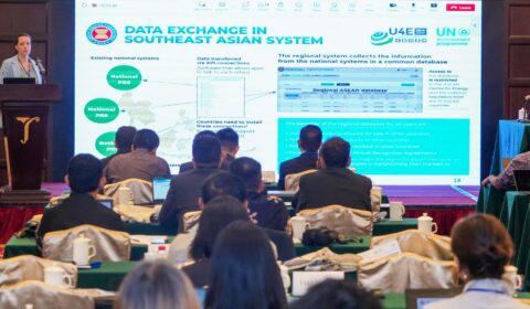 A woman presents to an audience in a conference room, with a large screen displaying Data Exchange in Southeast Asian System and related charts and text.