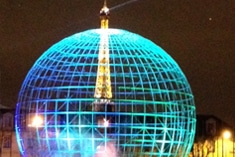 A glowing blue wireframe sphere structure with a lit tower, resembling the Eiffel Tower, at its center, set against a night sky.